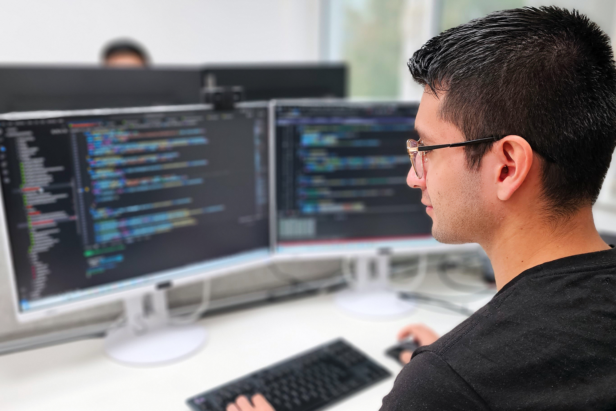 Bild: Softwareentwicklung. Ein junger dunkelhaariger Mann programmiert an einem Computer.