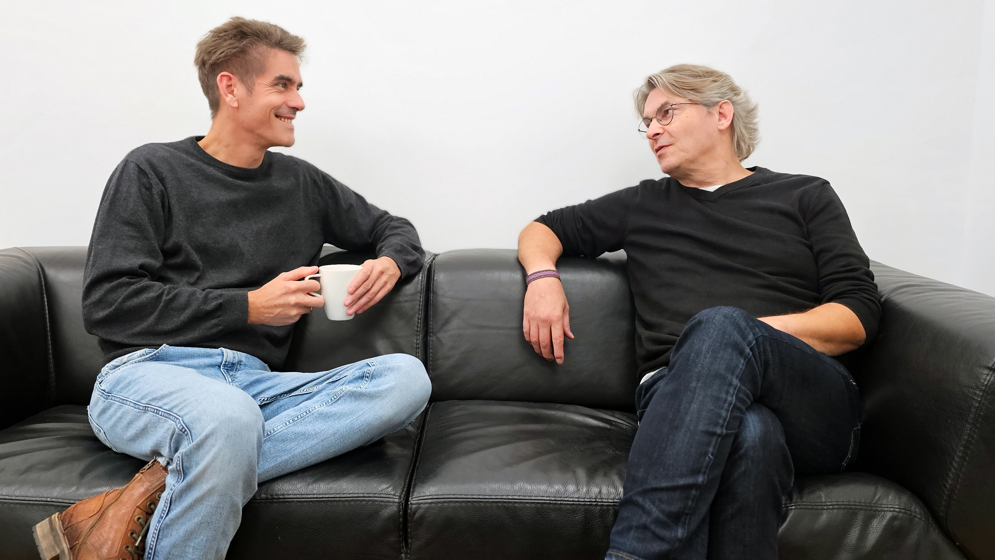 Foto der octasys-Geschäftsleitung. Die Geschäftsführer Torsten Brinkmann und Thomas Bäumken sitzen auf einem schwarzen Sofa und sprechen, zueinander gewandt, miteinander.